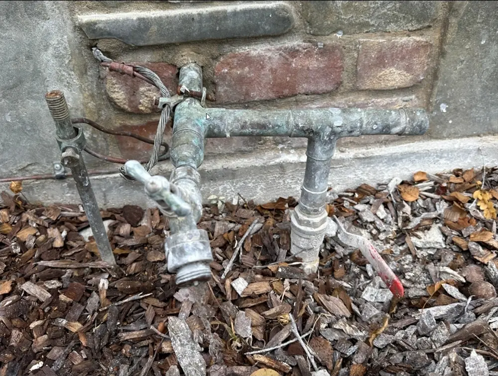 Old plumbing assembly with outdated pressure regulator, shutoff valve, and corroded exterior water supply piping causing excessive residential water pressure issues.