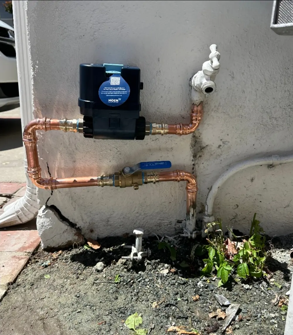 Smart automatic water shutoff valve installed on a residential main water line with copper piping and mobile app monitoring to provide leak detection and flood protection.
