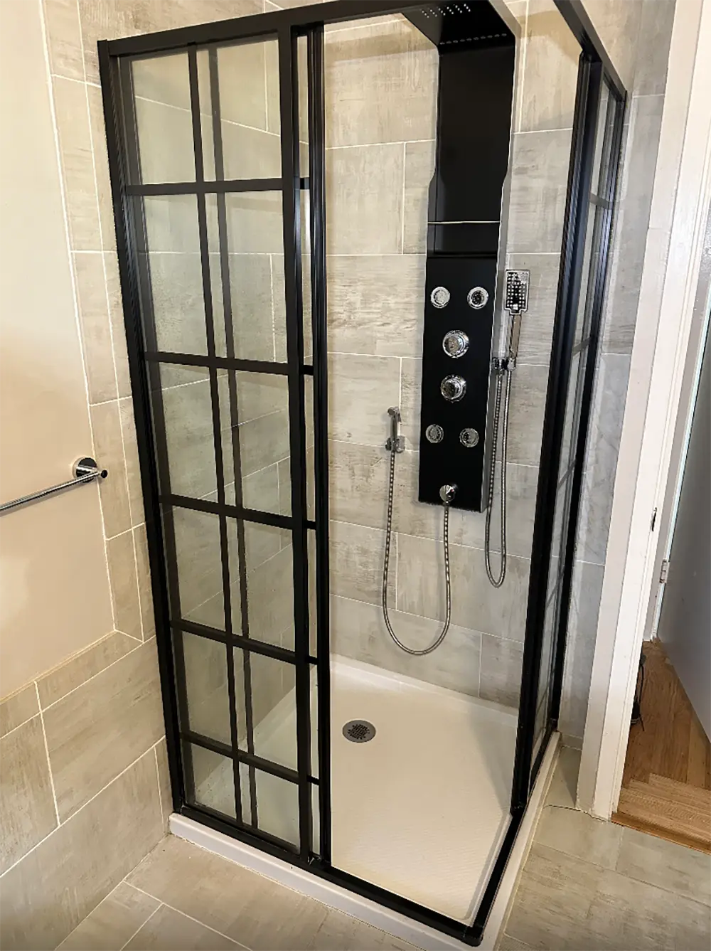 Modern shower panel tower installation with rainfall shower system, handheld shower wand, body spray jets, and black-framed glass enclosure in a contemporary bathroom.