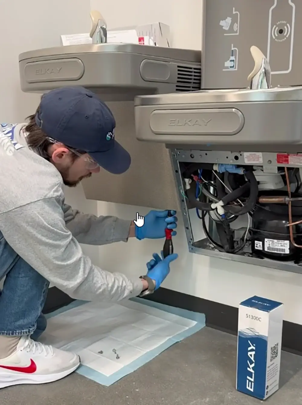 Technician replacing an Elkay drinking water filter cartridge inside a bottle filling station after shutting off the water supply and accessing the filtration system.