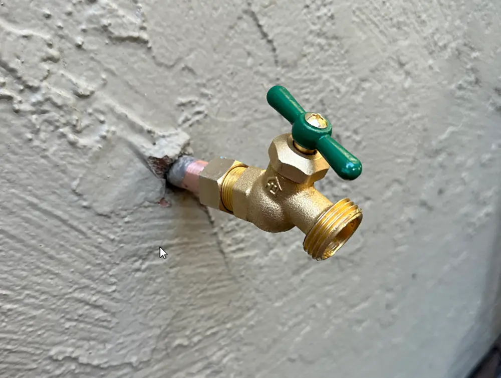 Old outdoor hose bib with traditional multi-turn valve and washer-based mechanism installed on exterior wall prior to replacement, showing aging plumbing fixture requiring upgrade.