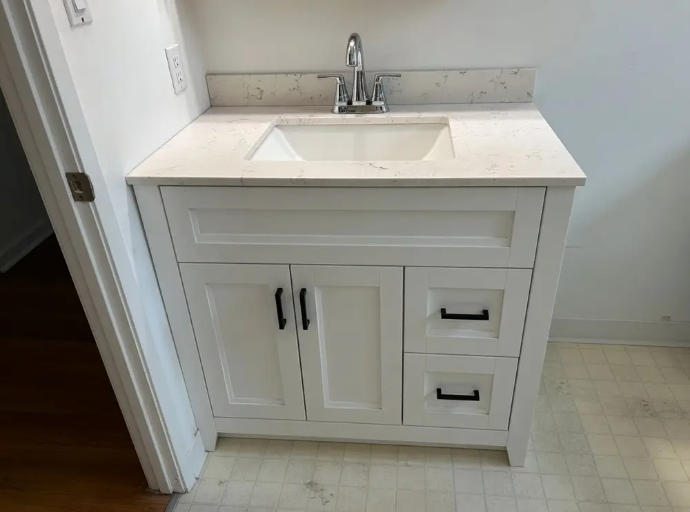 Modern white bathroom vanity installation with quartz countertop, integrated sink, chrome faucet, decorative backsplash, and custom cabinetry professionally fitted and sealed for water protection.