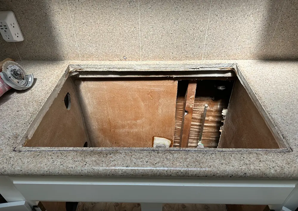 Kitchen sink removed during plumbing renovation, exposing cabinet interior and drain system prior to relocating an improperly positioned kitchen drain line.