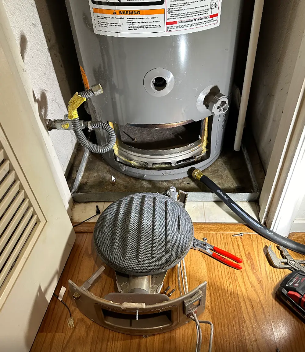 Gas water heater with removed burner assembly and faulty gas control valve during repair, showing disassembled components prior to replacement and system restoration.