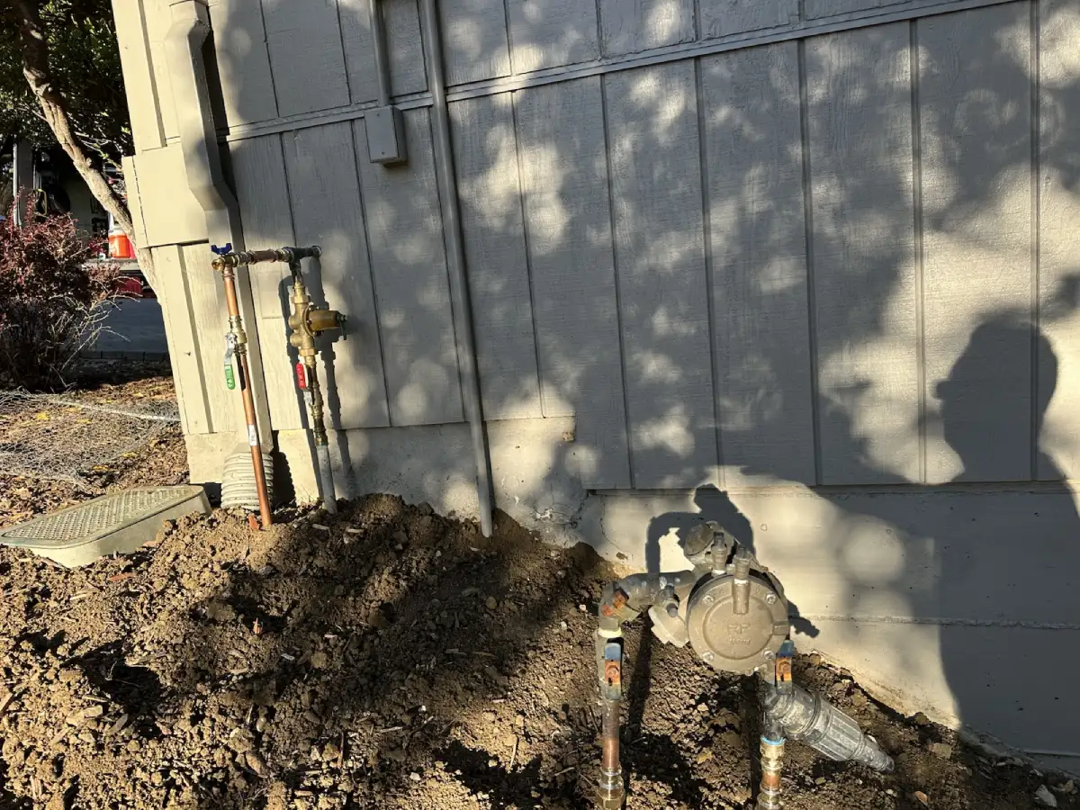 Exterior water line worksite with excavation and visible plumbing access near the building